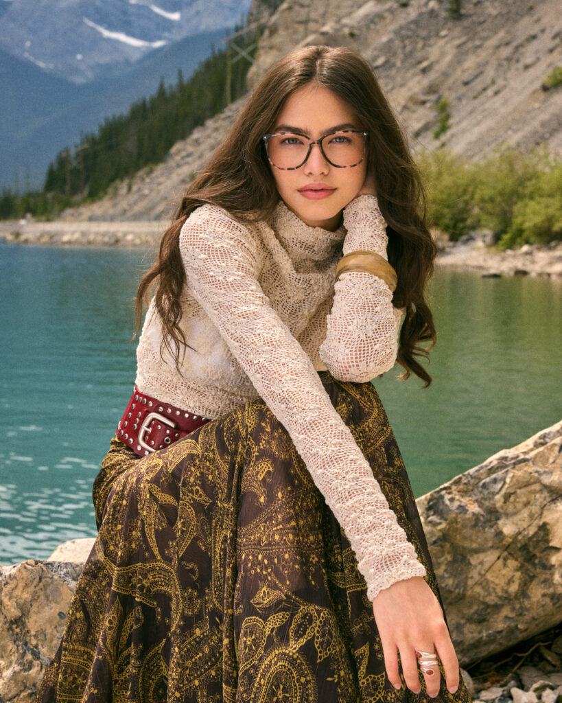 In a FW25 photoshoot for eyewear company Bonlook, model Ophélie of Folio management wearing a western inspired outfit, sitting by a lake with tall mountains in the background. Shot in the Canadian West. Styled by Gabriel Dupuis, hair and makeup by Nicole Saxton and photographed by Megane Brunette.