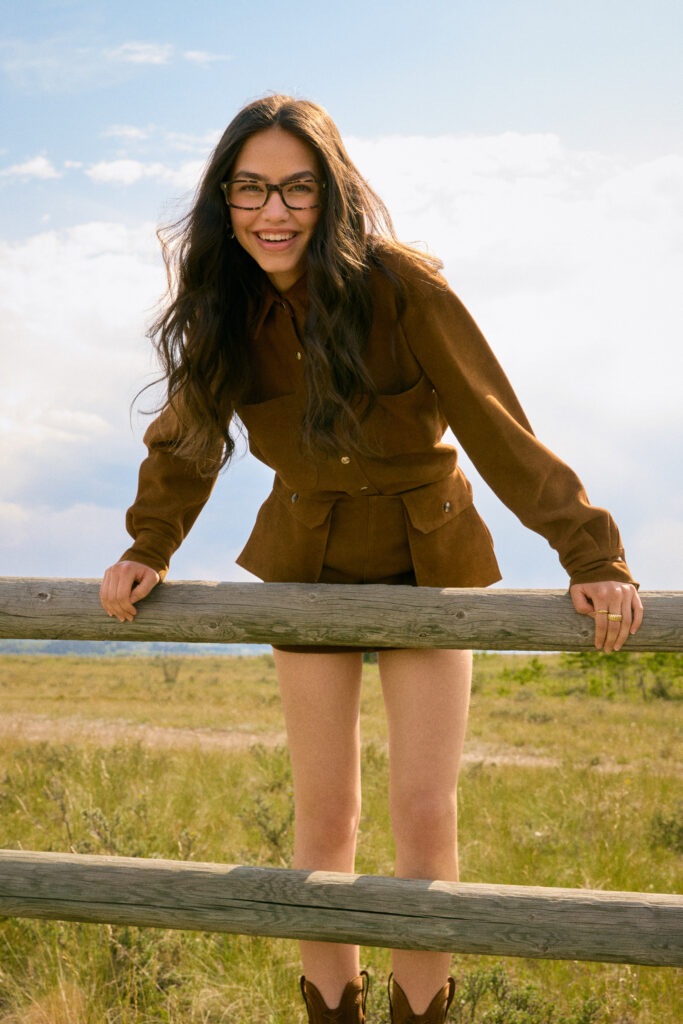 In a FW25 photoshoot for eyewear company Bonlook, model Ophélie of Folio management wearing a western inspired outfit leaning on a fence, shot in the Canadian West. Styled by Gabriel Dupuis, hair and makeup by Nicole Saxton and photographed by Megane Brunette.